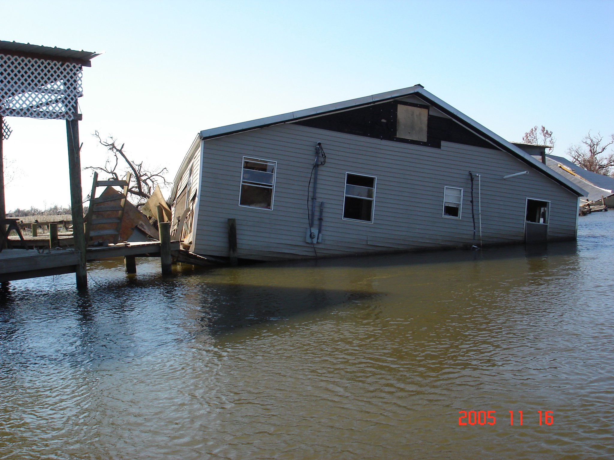Image of a sinking building. The building is halfway sunken in flood water. At the corner it says 2005. 